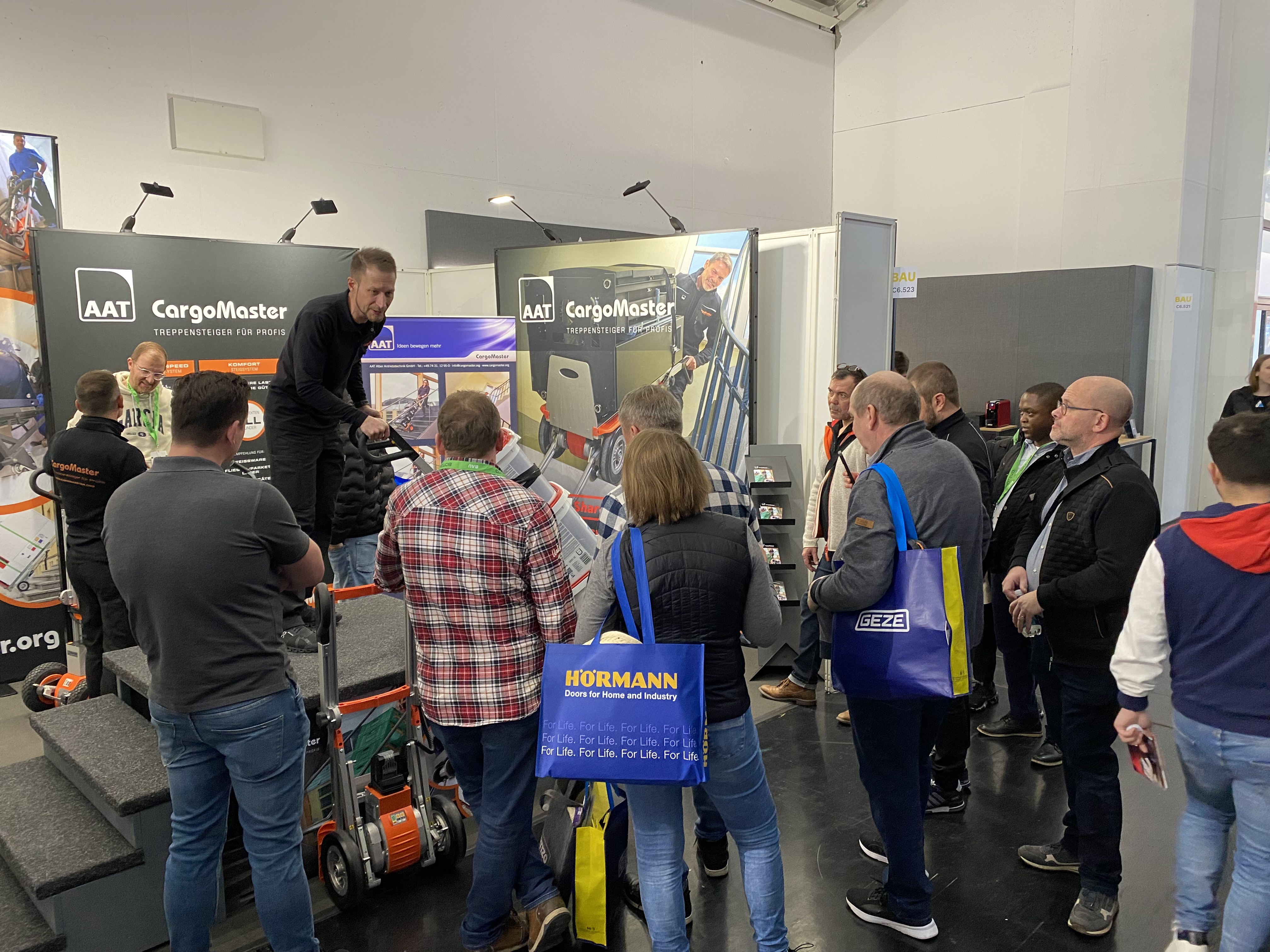 Das Bild zeigt einen unserer Mitarbeiter an unserem Messestand, der interessierten Besuchern unsere Geräte Cargomaster vorstellt.