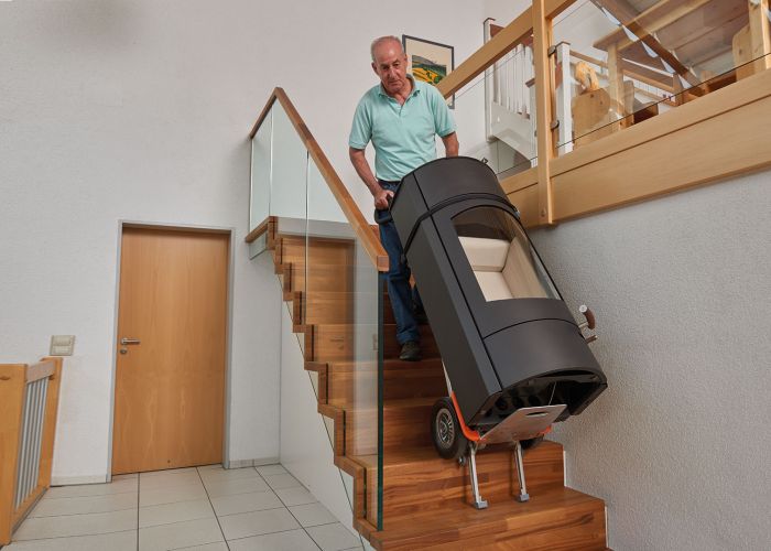 Das Bild zeigt den Einsatz des CargoMaster Treppensteigers mit einer speziellen Halterung für runde Güter. Gezeigt wird, wie ein runder Ofen über Treppen befördert wird.