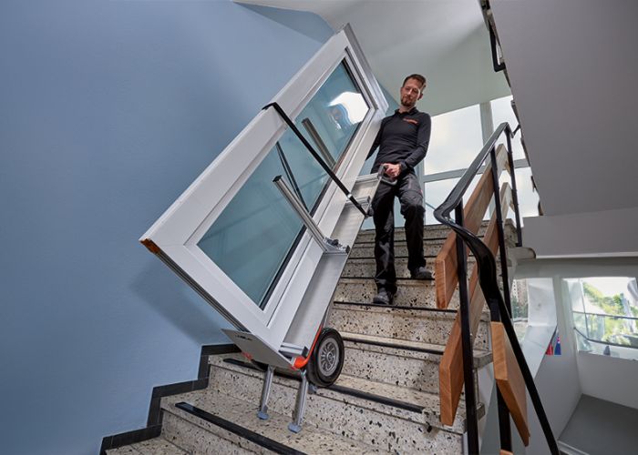 Das Bild zeigt den Einsatz des CargoMaster Treppensteigers mit einer speziellen Halterung für Türen und Fenster. Gezeigt wird, wie eine große Glastür über Treppen befördert wird.