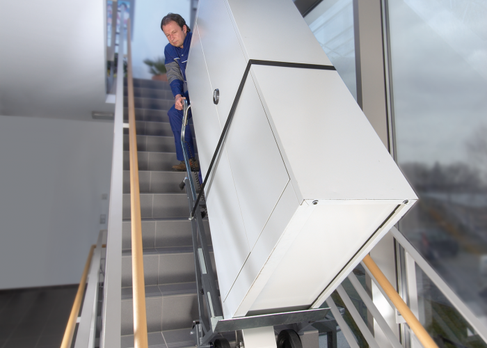 The picture shows the CargoMaster stair climber being used to transport a large cupboard up modern stairs in a town hall. 