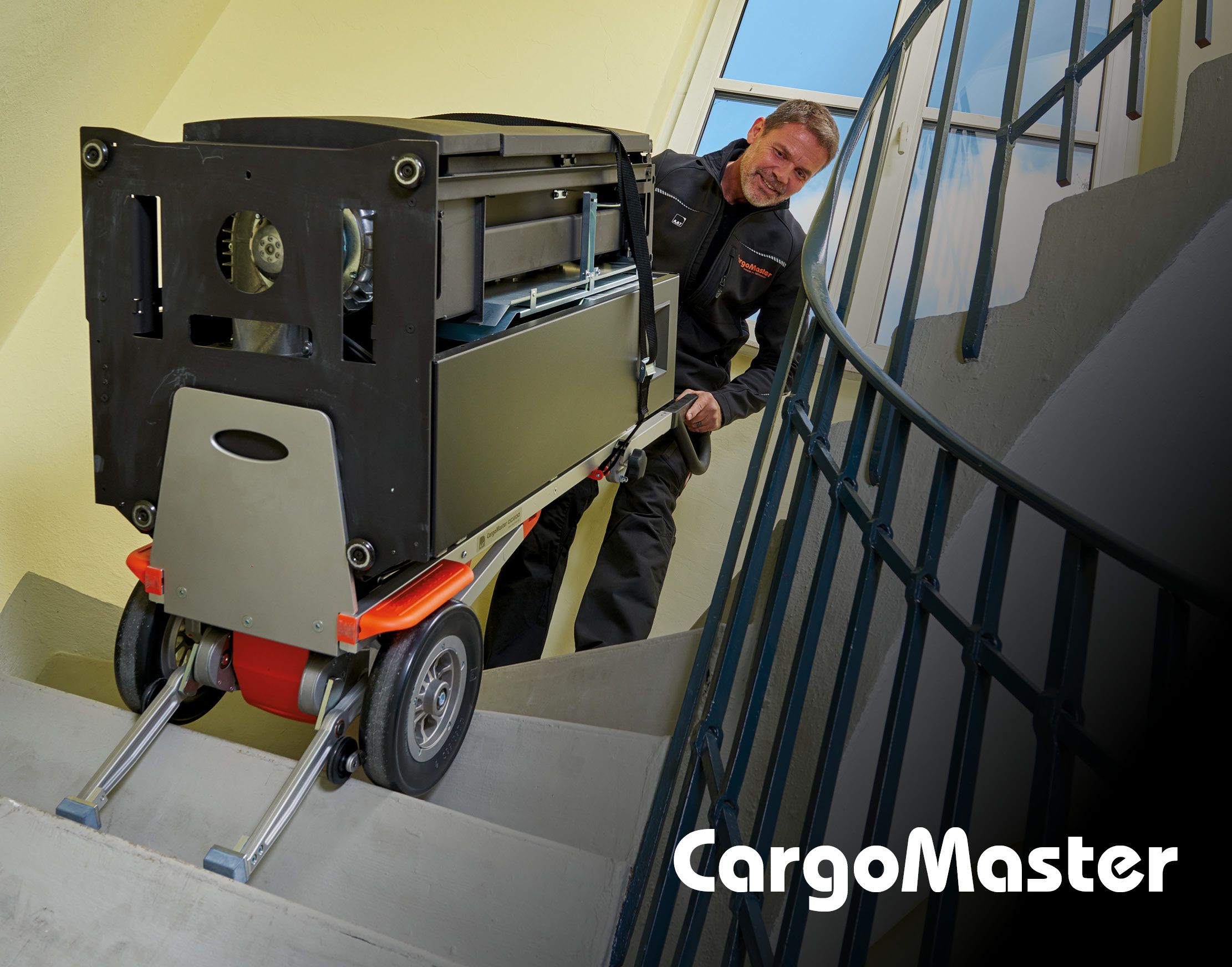 L'immagine mostra un dipendente di un'azienda che trasporta un forno pesante su per una scala con l'aiuto di un montascale elettrico CargoMaster di AAT. 