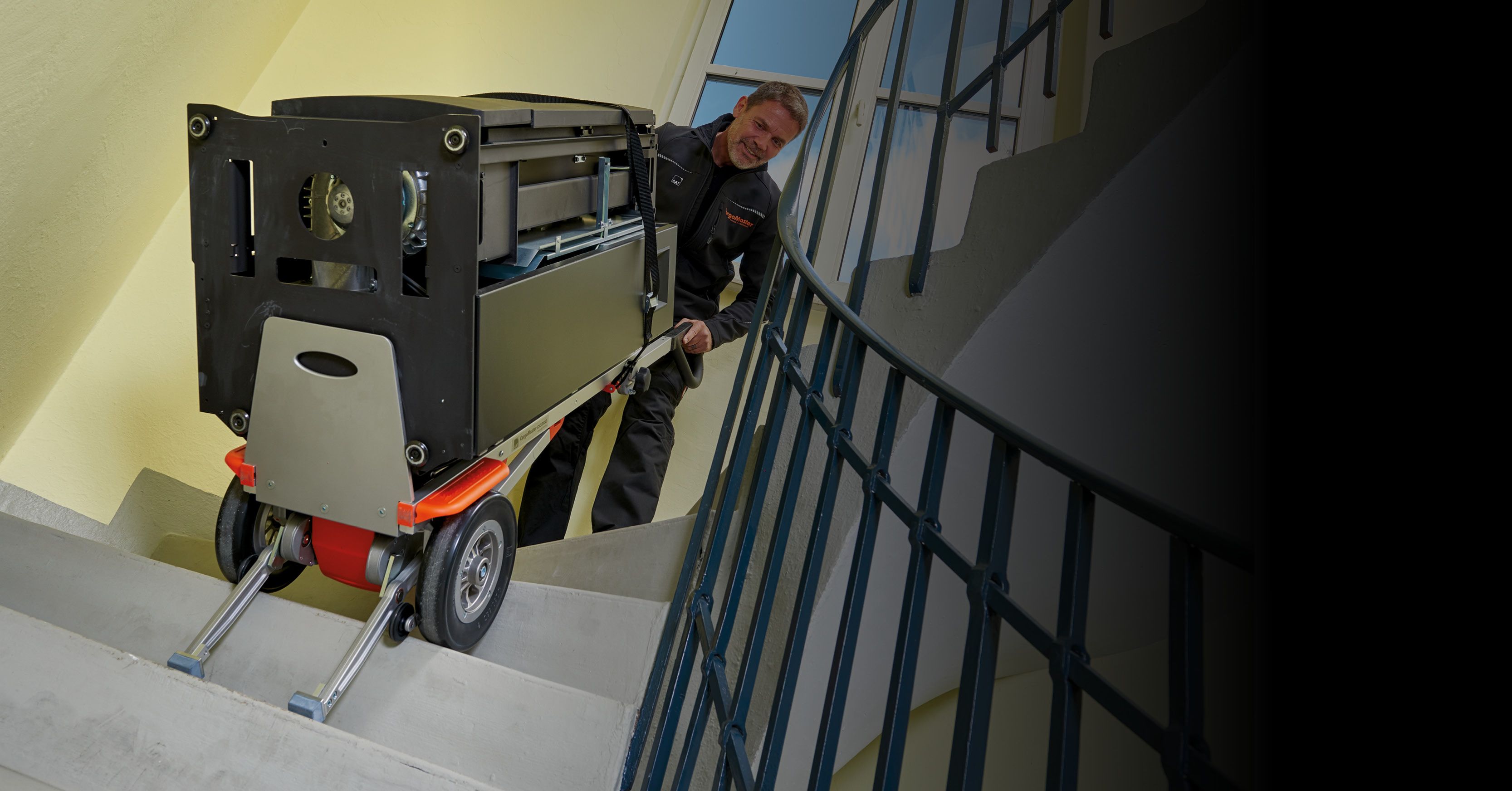 The picture shows an employee of a stove retailer effortlessly transporting a heavy stove up a staircase with the help of a CargoMaster CC200 mobile stair climber.