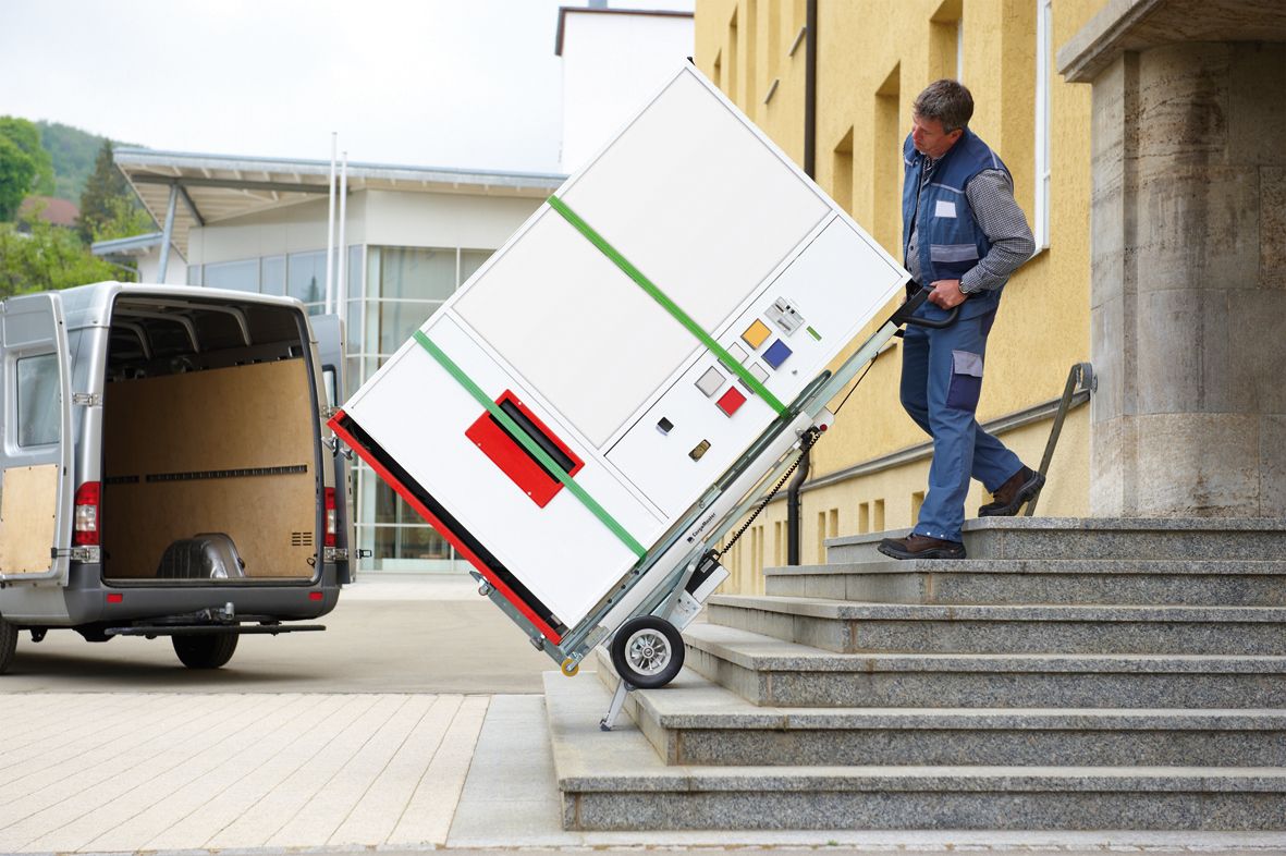 Auf dem Bild ist ein Mann zu sehen, der mit einem Treppensteiger CargoMaster große und schwere Weißware eine Außentreppe hinauf- oder hinab befördert. Er bedient den Treppensteiger alleine und braucht keine Unterstützung, um die schwere Last zu transportieren.